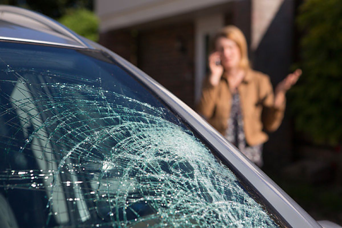 Severely shattered windshield on a parked car with the driver on the phone arranging a mobile auto glass replacement