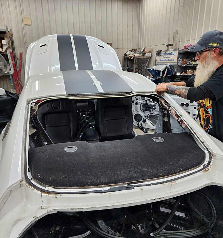 Technician removing the back glass from a white coupe with the pinchweld and old urethane bead exposed for inspection